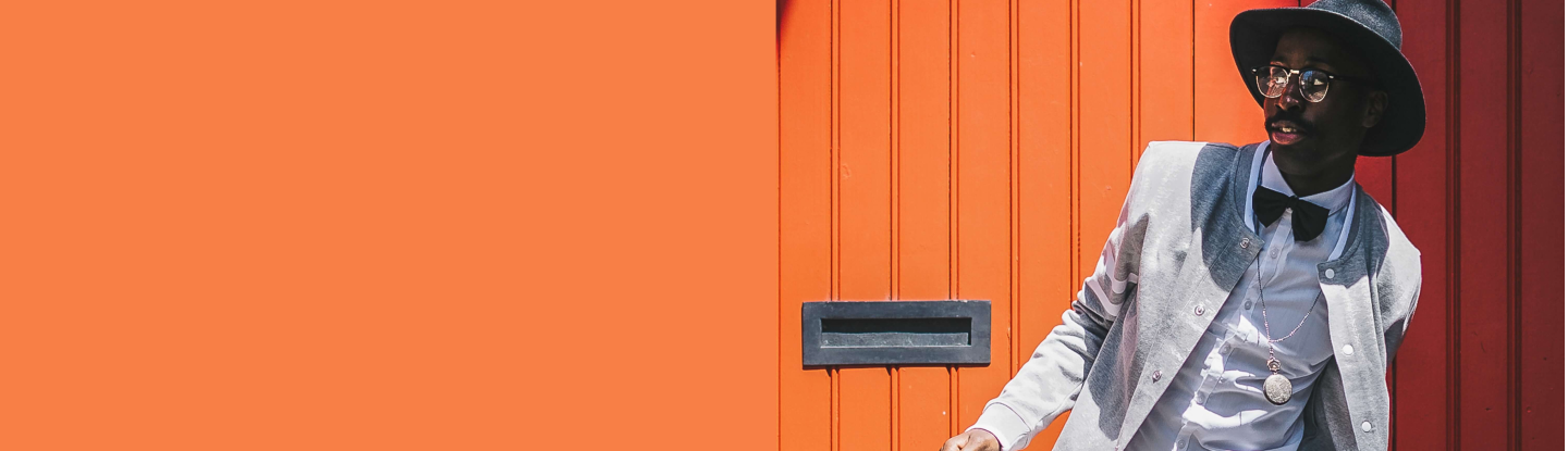 Modelo masculino vistiendo un traje plomo y camisa blanca, en fondo naranja