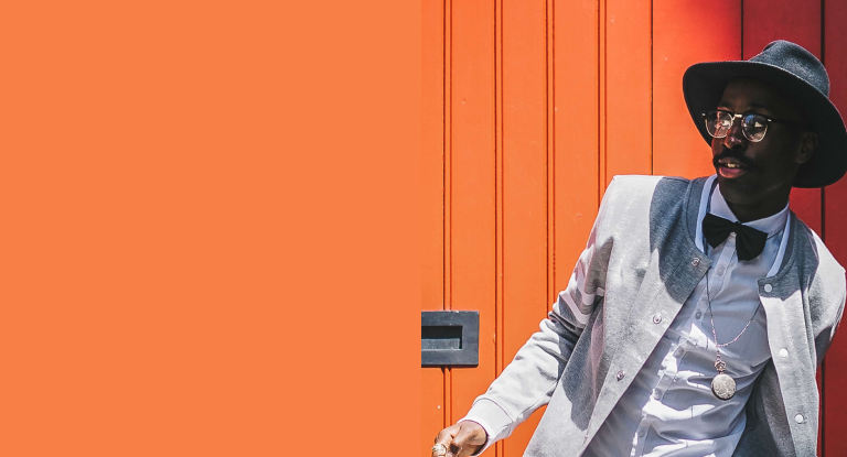Modelo masculino vistiendo un traje plomo y camisa blanca, en fondo naranja