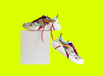 Par de zapatillas unisex con color predominante blanco y trazos en colores naranja, azul, verde y cordones rojos, sobre fondo verde limón