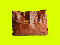 Bolsa femenina de cuero en color marrón, con cortes cuadrados y asa dorada en forma de cadena con detalle verde, sobre fondo verde limón